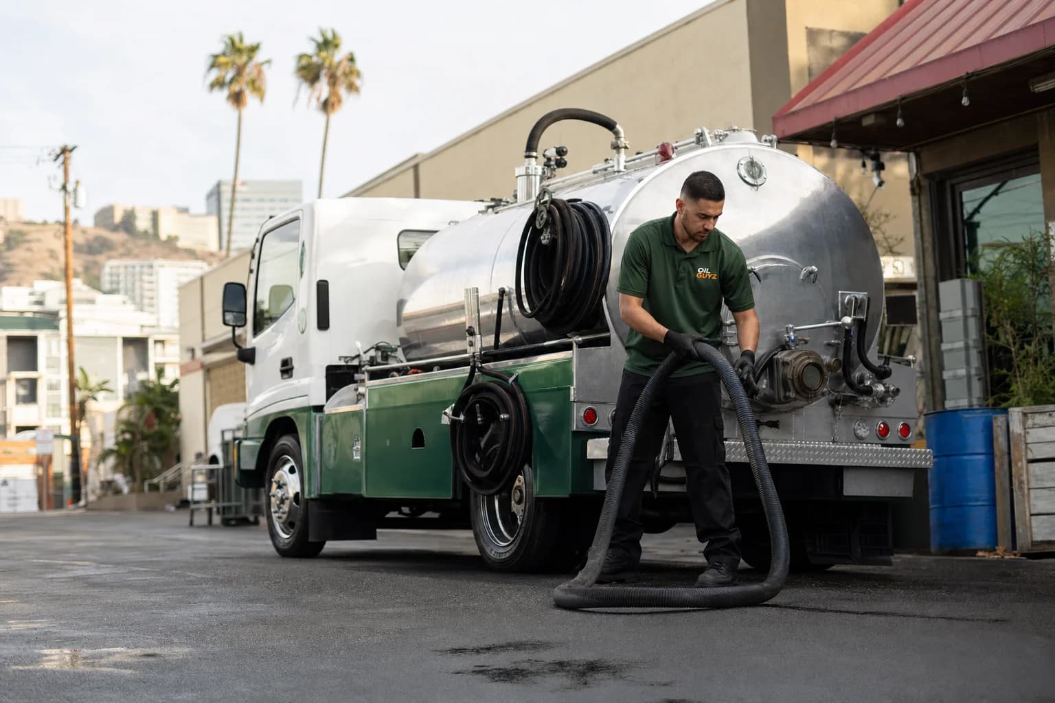 Free used cooking oil pickup at a Inglewood restaurant — unbranded white pump truck with hunter-green Oil Guyz technician