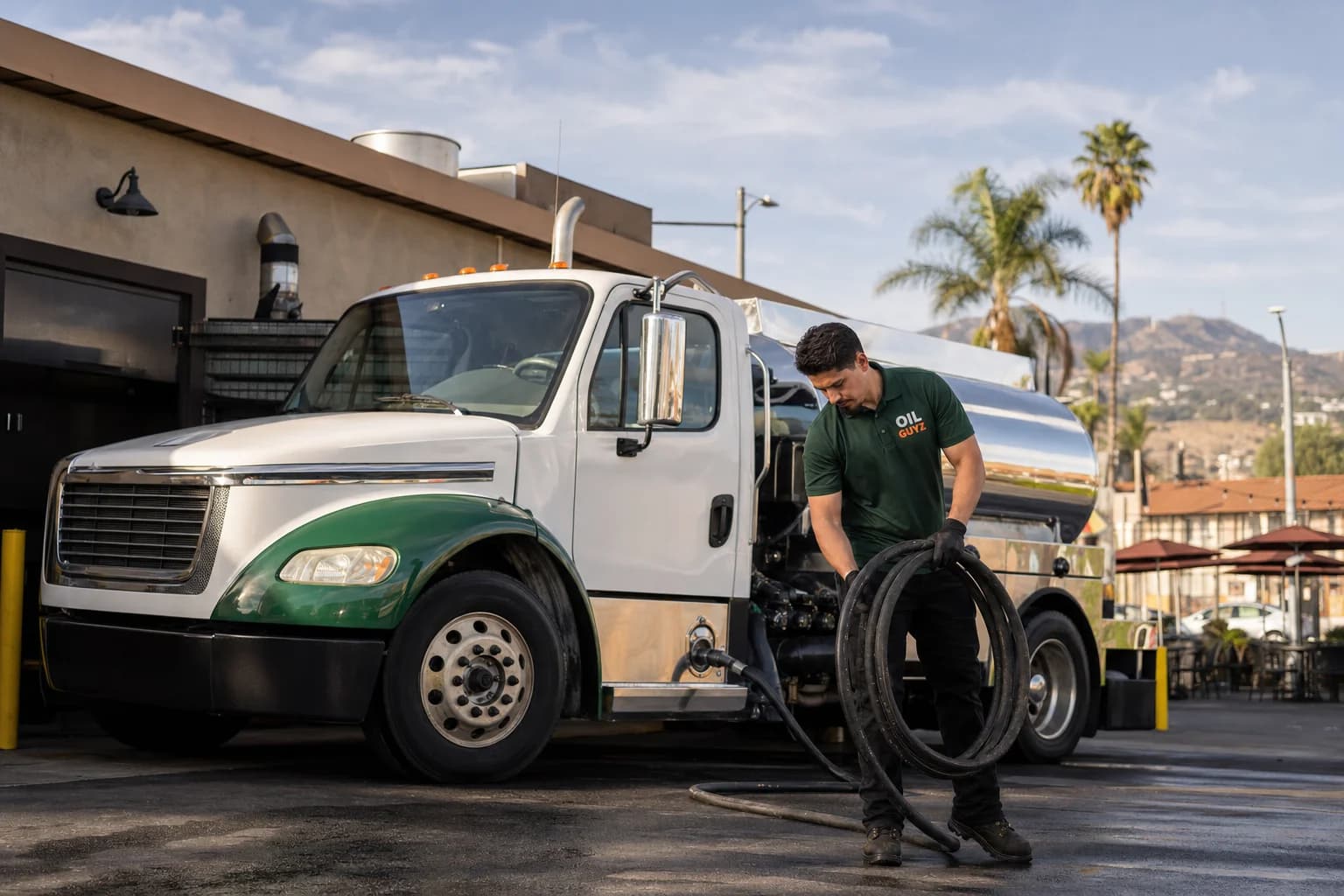Free used cooking oil pickup at a Pasadena restaurant — unbranded white pump truck with hunter-green Oil Guyz technician