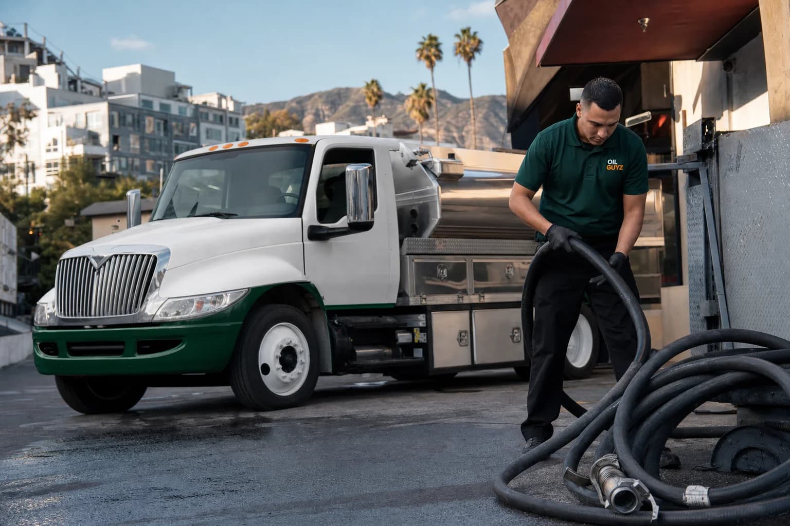 Free used cooking oil pickup at a Pomona restaurant — unbranded white pump truck with hunter-green Oil Guyz technician