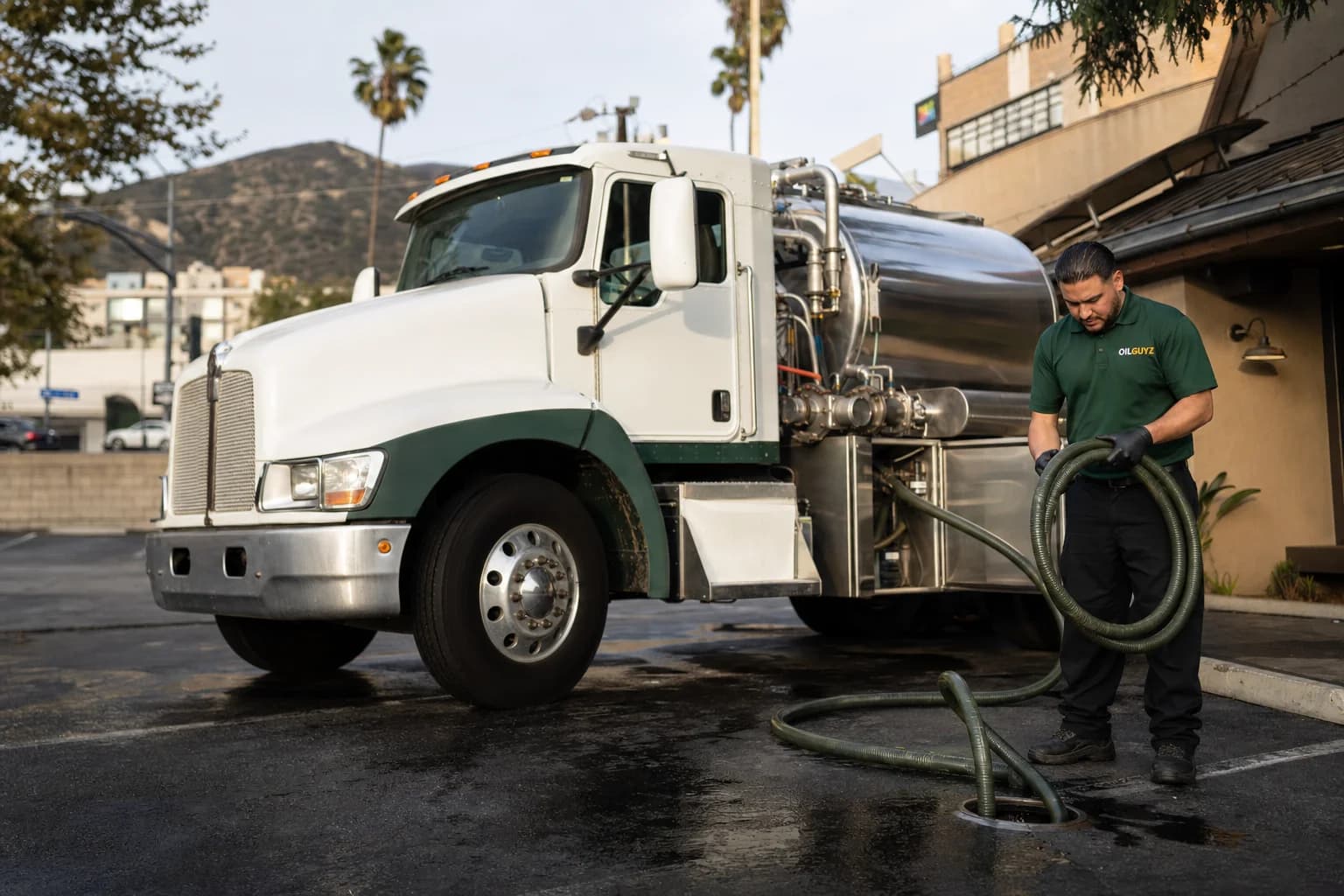 Free used cooking oil pickup at a San Dimas restaurant — unbranded white pump truck with hunter-green Oil Guyz technician