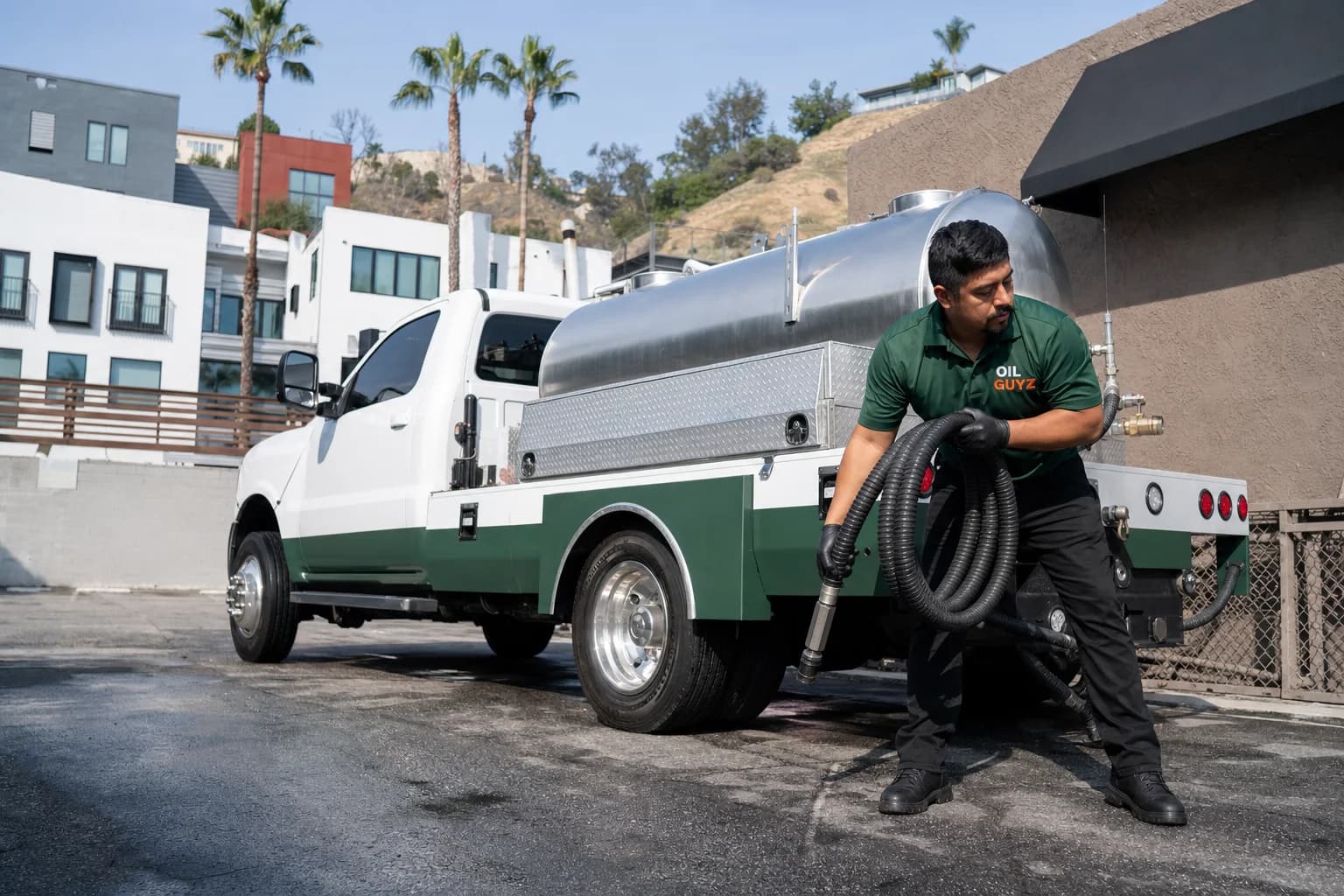 Free used cooking oil pickup at a West Covina restaurant — unbranded white pump truck with hunter-green Oil Guyz technician