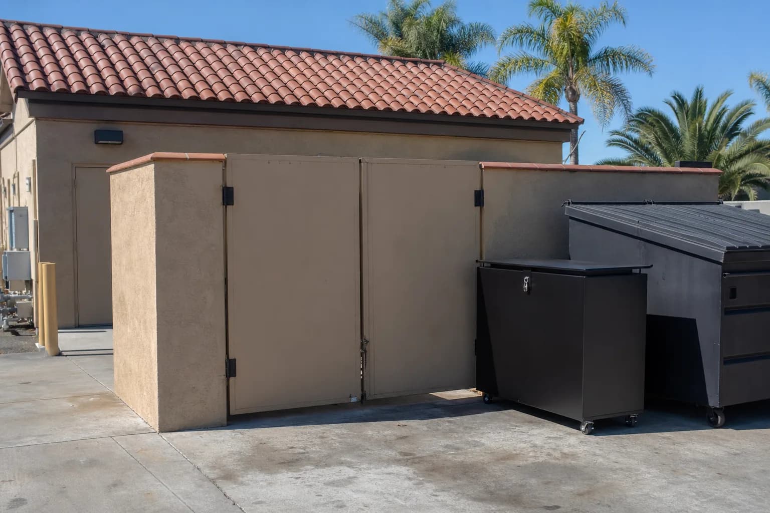 Locked black used cooking oil bin on the back dock of an Orange County restaurant, beside the open kitchen door with the fryer station visible inside