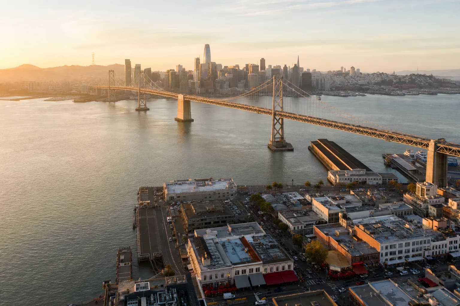 Aerial view of the San Francisco Bay Area waterfront and skyline at golden hour with bridges connecting the East Bay and Peninsula
