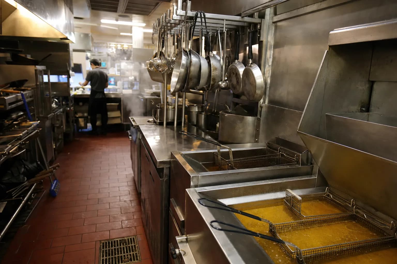 Back-of-house fry station in a busy Fremont restaurant kitchen with stainless steel deep fryers, prep counters, and a floor drain, no text or logos