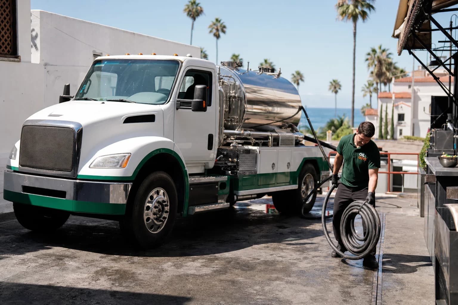 Free used cooking oil pickup at a Coronado restaurant — unbranded white pump truck with hunter-green Oil Guyz technician