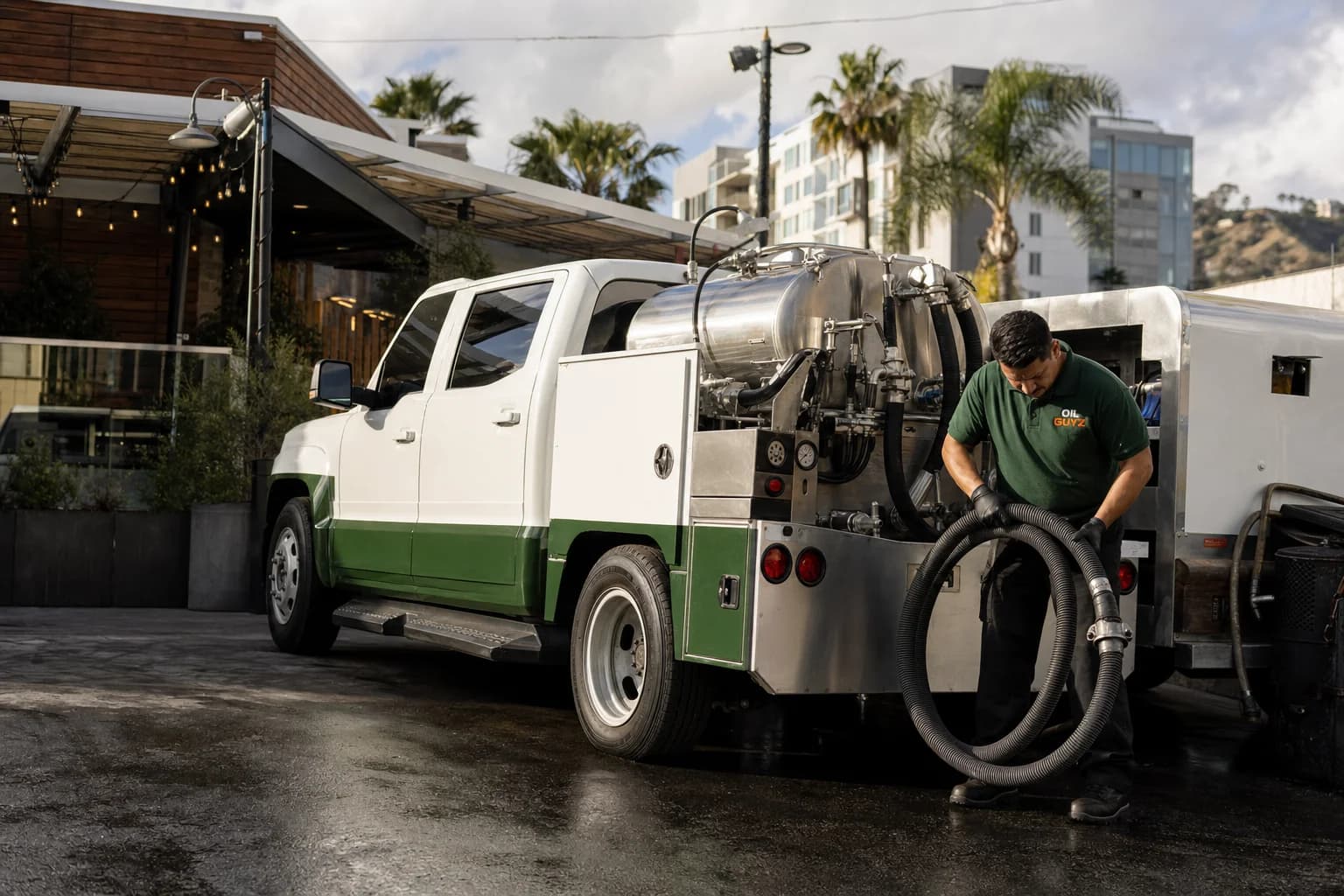 Free used cooking oil pickup at a El Segundo restaurant — unbranded white pump truck with hunter-green Oil Guyz technician