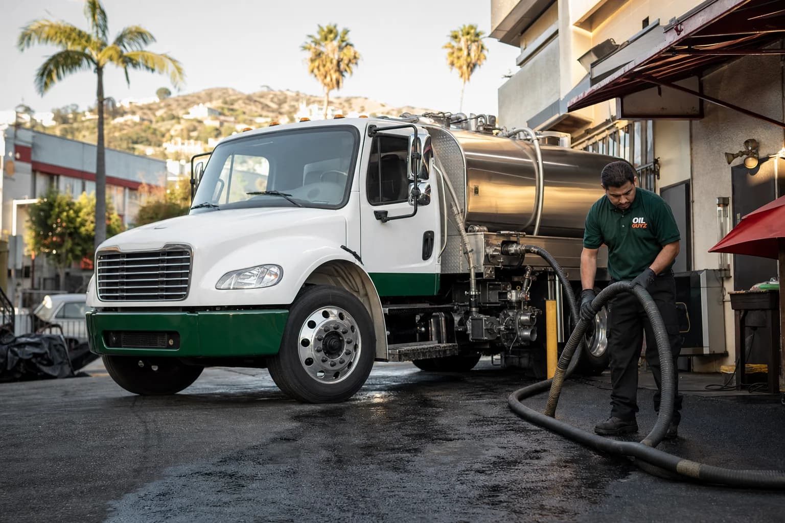 Free used cooking oil pickup at a Monterey Park restaurant — unbranded white pump truck with hunter-green Oil Guyz technician
