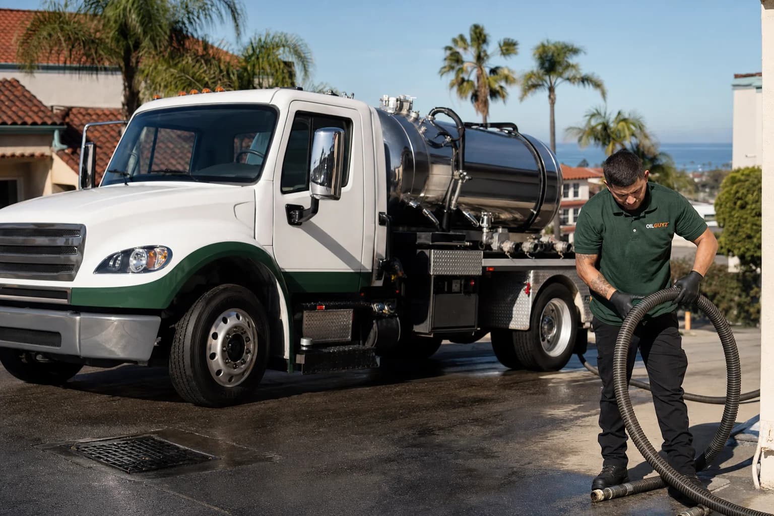 Free used cooking oil pickup at a National City restaurant — unbranded white pump truck with hunter-green Oil Guyz technician
