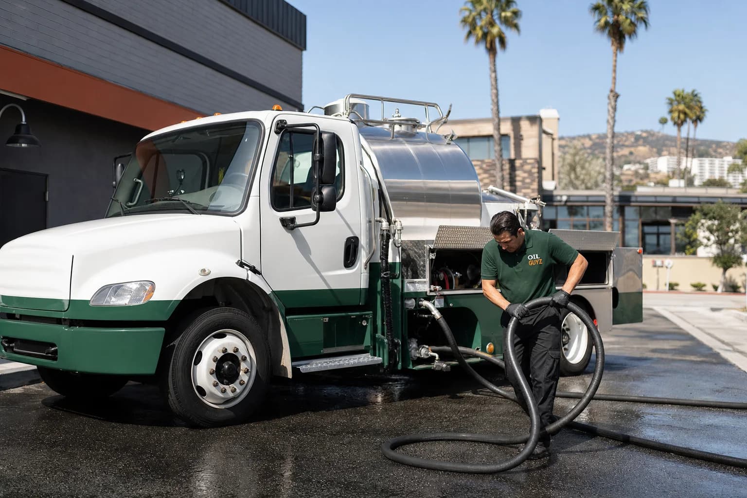 Free used cooking oil pickup at a Palmdale restaurant — unbranded white pump truck with hunter-green Oil Guyz technician