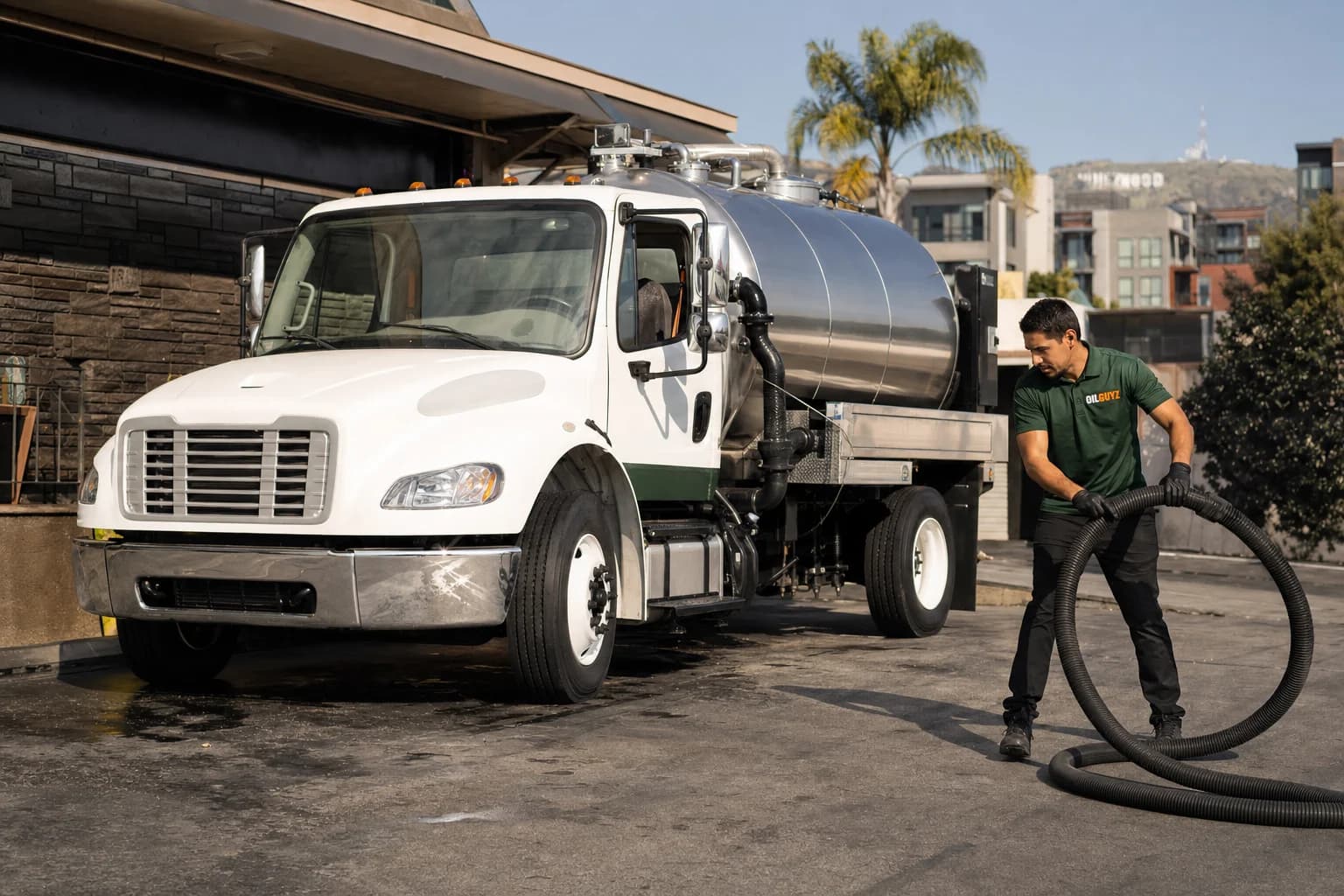 Free used cooking oil pickup at a Paramount restaurant — unbranded white pump truck with hunter-green Oil Guyz technician