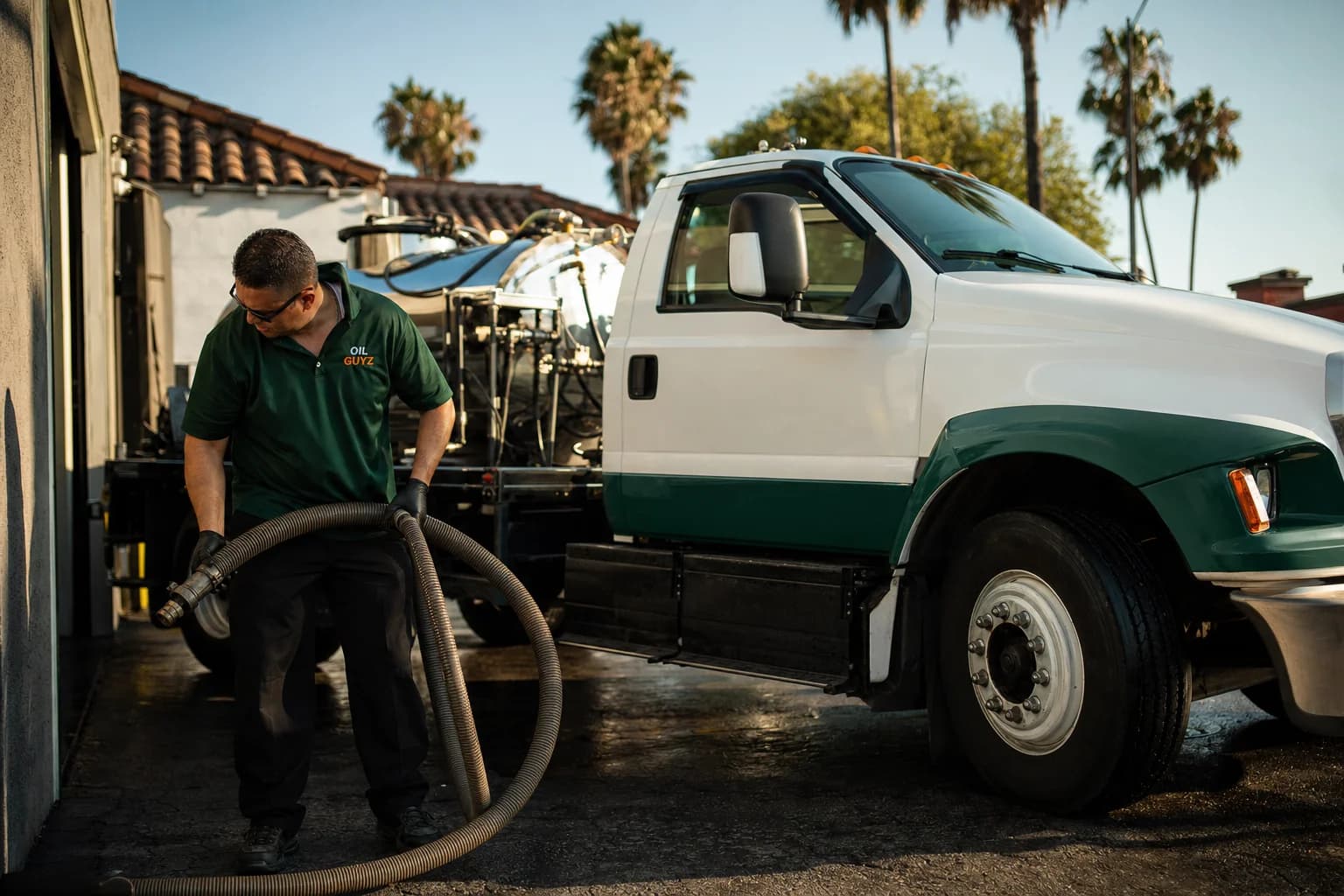Free used cooking oil pickup at a Tustin restaurant — unbranded white pump truck with hunter-green Oil Guyz technician